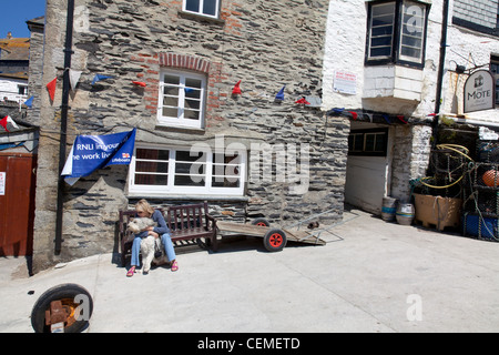 Port Isaac à Cornwall en Angleterre, lady s'assit sur un banc de travail avec chien à l'extérieur de pub dans village Banque D'Images