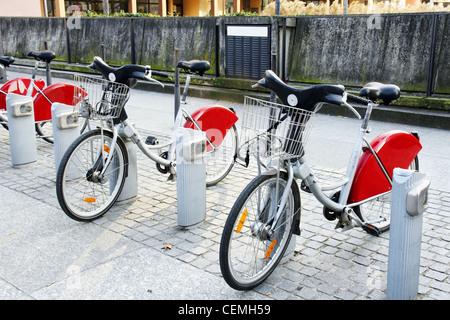 D'un autre moyen de transport : location de vélos garés à une gare en face de mur en béton dans la vieille ville européenne. Banque D'Images