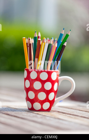 Des crayons de couleur rouge et blanc dans un mug à pois à l'extérieur sur une table en bois Banque D'Images
