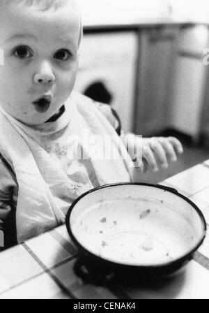 L'ALFI À LA MAISON' enfant assis à table avec bol vide, ayant fini son repas Banque D'Images