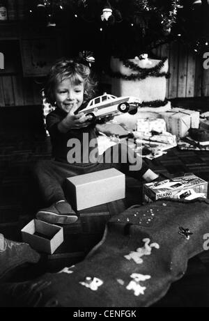 S'enfant mâle wearing pajamas assis sur flowith fort entre les jambes holding toy voiture de police dans les mains, à la voiture à sourire, Banque D'Images