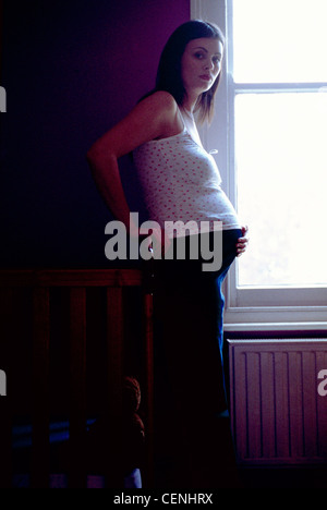 Profil des femmes enceintes fortement les cheveux longs brunette wearing jeans débardeur floral et la moitié dans l'ombre l'article dans la fenêtre Banque D'Images