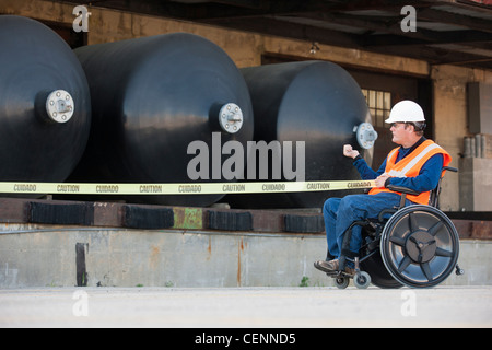 Ingénieur des installations en tirant un fauteuil roulant en face du ruban de réservoirs de stockage de produits chimiques Banque D'Images