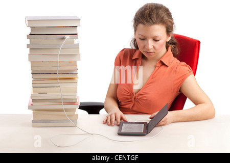 Jeune femme avec ebook reader qui est connecté avec une pile de livres Banque D'Images