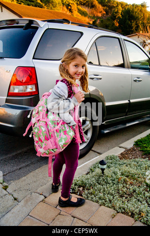 Portant son sac à dos et boîte à lunch, une fillette de 6 ans attend par la voiture pour aller à l'école à San Juan Capistrano CA. Communiqué de modèle Banque D'Images