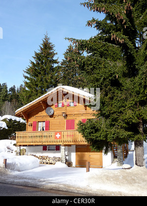 Brun et rouge clair ensoleillé chalet en bois au jura par l'hiver, en Suisse, en face de sapins Banque D'Images