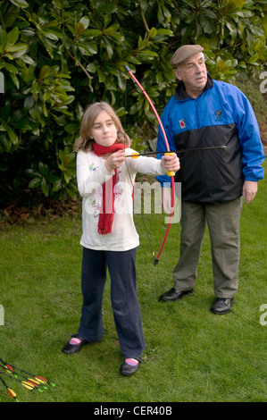 Une fillette de 9 ans joue avec un arc et une flèche supervisé par son grand-père Banque D'Images