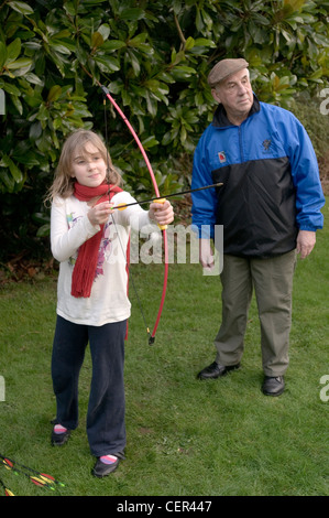 Une fillette de 9 ans joue avec un arc et une flèche supervisé par son grand-père Banque D'Images