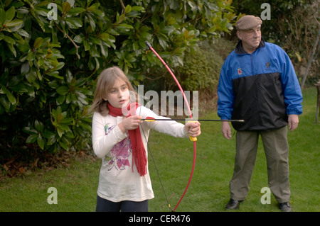 Une fillette de 9 ans joue avec un arc et une flèche supervisé par son grand-père Banque D'Images