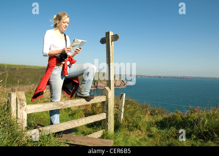 Une femelle Walker s'arrête à un stile à lire une carte au-dessus de la tête de Sainte Anne sur la côte de Pembrokeshire. Banque D'Images