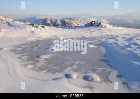 Tarn gelé sur Grand Knott, Crinkle Crags, avec les Langdale Pikes en arrière-plan, l'hiver dans le Lake District Banque D'Images