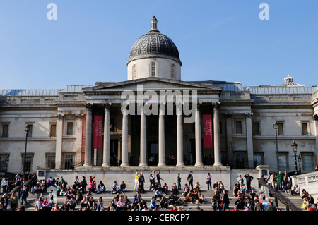 Les gens assis sur les marches à l'extérieur de la National Gallery à Trafalgar Square. Banque D'Images
