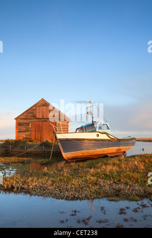 Un bateau amarré par l'ancien hangar du charbon à la première lumière à Thornham Harbour sur la côte nord du comté de Norfolk. Banque D'Images