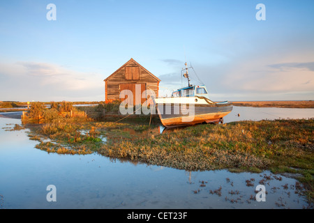 Un bateau amarré par l'ancien hangar du charbon à la première lumière à Thornham Harbour sur la côte nord du comté de Norfolk. Banque D'Images