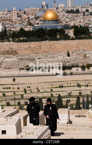 Les hommes juifs orthodoxes marche à travers le cimetière juif sur le Mont des Oliviers à Jérusalem. Banque D'Images
