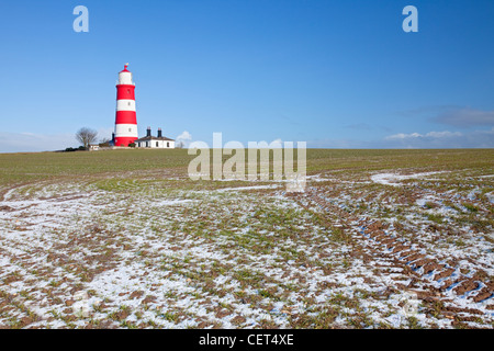 Neige de l'hiver dans un champ par Happisburgh phare, le plus vieux phare de travail dans l'East Anglia. Banque D'Images