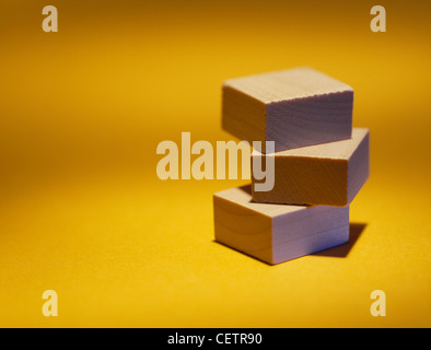 Trois blocs de construction en bois empilés sur un fond jaune lumineux Banque D'Images