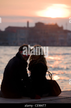 Couple sitting in venice portant des masques de mascarade au coucher du soleil Banque D'Images
