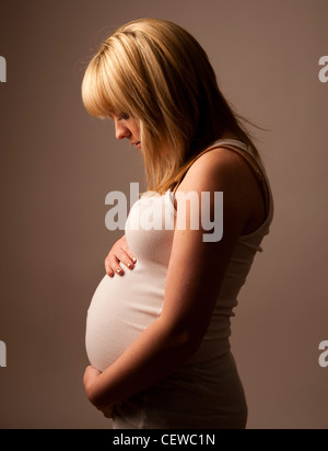 Un profil d'un adolescent aux cheveux blonds enceinte fille jeune femme tenant son ventre et regardant vers le bas Banque D'Images