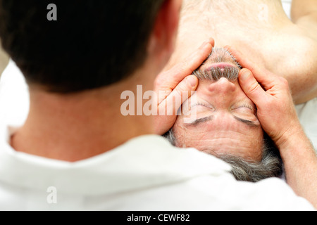 Massothérapeute le massage du visage d'un homme pose face visible sur la table. Homme mûr face se masser par un massothérapeute masculin à un spa. Banque D'Images