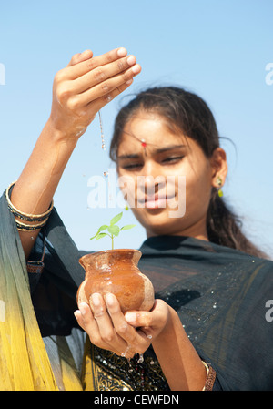 Indian girl aspersion de l'eau sur un semis de plantes dans un pot en argile. L'Inde Banque D'Images