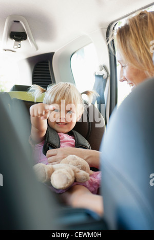 Little girl pointing et sourire comme sa mère maintient son siège de voiture en Banque D'Images