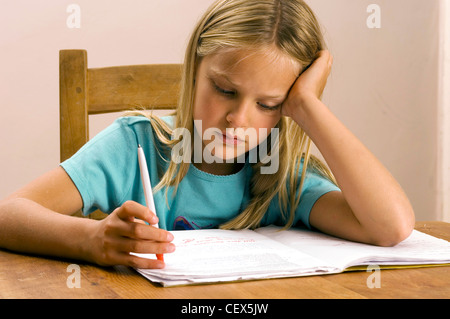 Enfant de sexe féminin était assis à une table en bois à faire leurs devoirs, s'appuyant sa tête sur sa main Banque D'Images