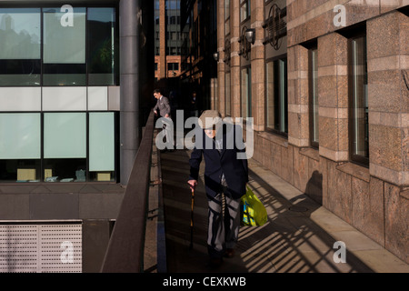 Homme âgé promenades le long de la passerelle moderne, passé une jeune employée de bureau bénéficiant d'un moment thoughful dans City of London. Banque D'Images