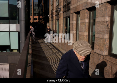 Homme âgé promenades le long de la passerelle moderne, passé une jeune employée de bureau bénéficiant d'un moment thoughful dans City of London. Banque D'Images