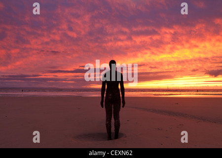 Firey Coucher de soleil sur Crosby Beach, avec l'une des statues d'Antony Gormley qui se profile. Banque D'Images