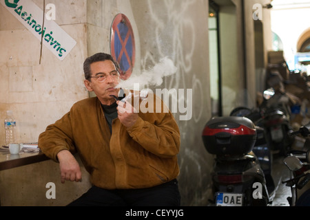 Un homme s'allume et fume une pipe à l'extérieur d'un petit café dans le marché central d'Athènes sur Athinas Street. Athènes, Grèce Banque D'Images