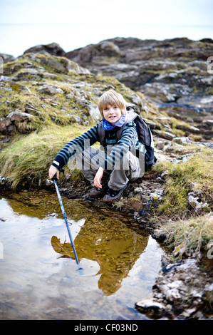 Jeune garçon dans des bottes et portant un sac à dos heureusement explore des rochers sur un champ de la géographie de l'école voyage dans le Devon Banque D'Images