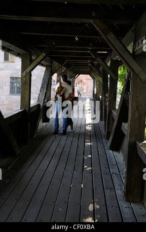 Un couple de touristes sur la passerelle en bois appelée "la promenade de l'exécuteur" à travers la rivière Pegnitz à Nuremberg, en Allemagne. La longue mosaïque rouge Banque D'Images