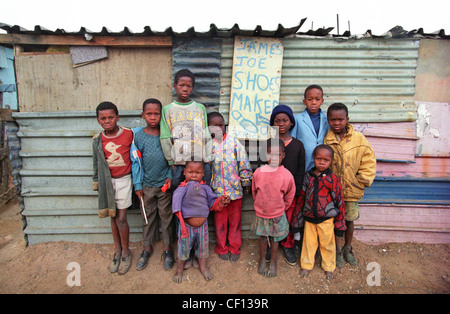 Les jeunes garçons, certains pieds nus, posent devant James Joe Shoe maker's shack à Soweto, en Afrique du Sud. Banque D'Images