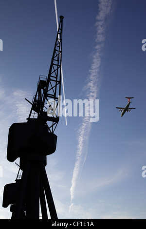 Un avion survolant la silhouette d'une grue à l'abandon au Royal Victoria Dock dans le réaménagement des Docklands de Londres. Banque D'Images