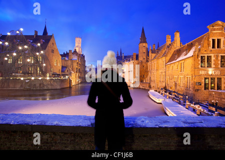 Une dame dans un manteau chaud et blanc bobble hat donne sur une vue de Rozenhoedkaai avec un canal gelé et la neige Banque D'Images