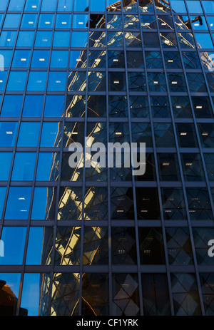 30 St Mary Axe, aussi connu sous le Gherkin, reflétée dans les fenêtres d'un immeuble de bureaux. Banque D'Images