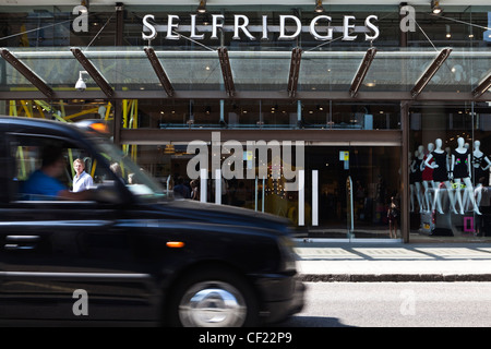 Un taxi Londres noir passant l'entrée de Selfridges sur Oxford Street. Banque D'Images