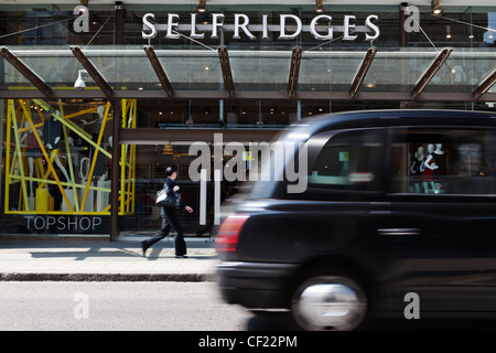Un taxi Londres noir passant l'entrée de Selfridges sur Oxford Street. Banque D'Images