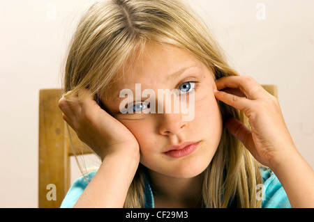 Enfant de sexe féminin était assis à une table en bois s'appuyant sa tête sur sa main Banque D'Images