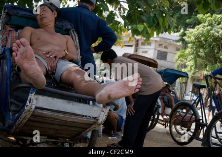 Un homme dort dans un cyclo sur un trottoir ombragé à Phnom Penh, Cambodge. Banque D'Images