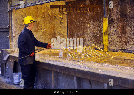 Un travailleur de l'acier d'écumage et prépare le zinc fondu à une usine de galvanisation. Banque D'Images