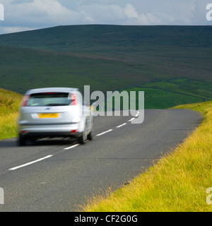 Une voiture roulant le long d'une route de campagne qui traverse un paysage spectaculaire, dans le Pennine North Pennines Zone d'une beauté exceptionnelle Banque D'Images