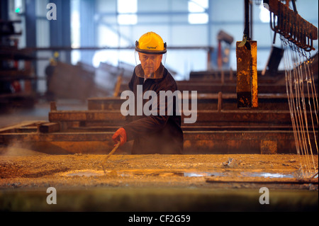 Un travailleur de l'acier d'écumage et prépare le zinc fondu à une usine de galvanisation. Banque D'Images