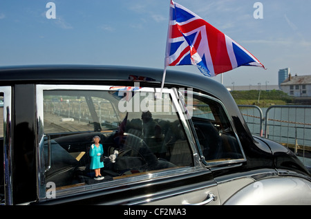 Une petite figure de la reine Elizabeth II dans la fenêtre d'une voiture classique et un drapeau de l'Union européenne fixée à l'extérieur. Banque D'Images