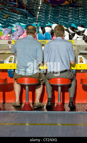 Deux hommes assis sur des tabourets de jouer à un jeu à une foire sur la jetée de Brighton. Banque D'Images