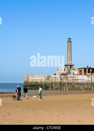 Les promeneurs de chiens sur la plage de sable à marée basse avec phare de Margate dans l'arrière-plan. Banque D'Images