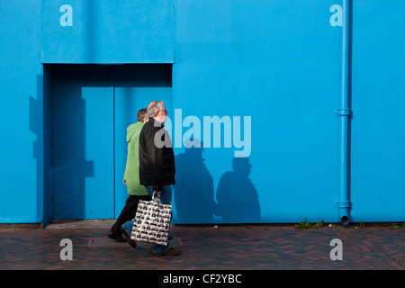 L'homme et de la femme marchant portant un panier d'ombres sur un mur bleu. Banque D'Images