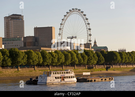 Les passagers d'un bateau amarré sur la Tamise avec le London Eye en arrière-plan. Banque D'Images
