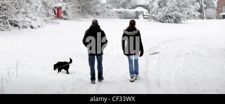 Marcher sur la couverture de neige le long de la route de campagne un homme et une femme couple faisant la promenade de chien du matin après de fortes chutes de neige d'hiver Brentwood Essex Angleterre Royaume-Uni Banque D'Images